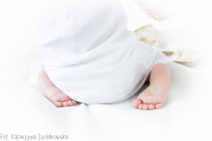 Fotografia niemowlęca. Sesja dziecięca w Krakowie. zdjęcie przedstawia stópki dziesieciomiesięcznej dziewczynki w białej sukience.