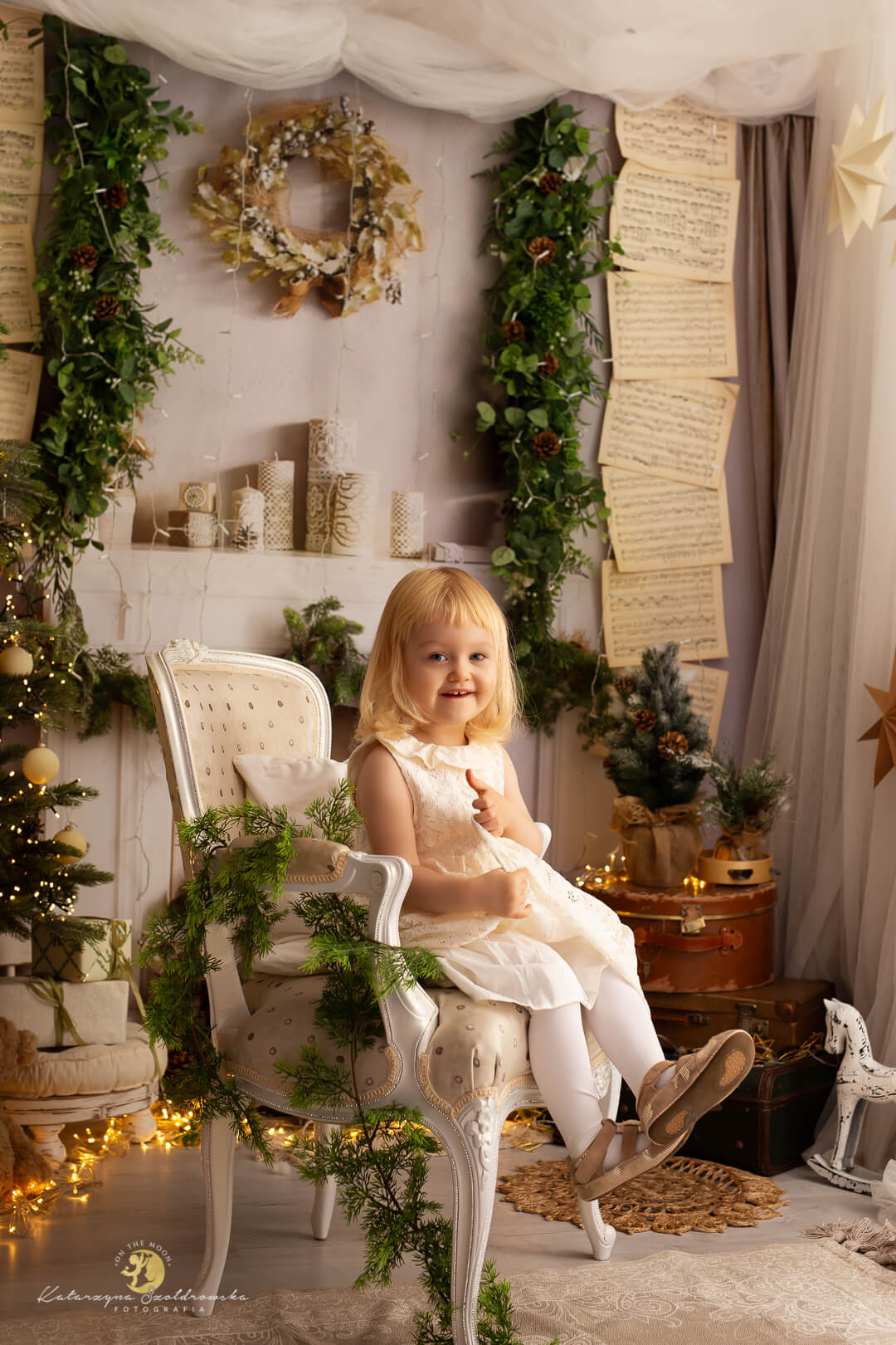 Kraków sesja świateczna. Zdjęcie z sesji śewiatecznej małej dziewczynki siedzącej na fotelu na tle białego kominka