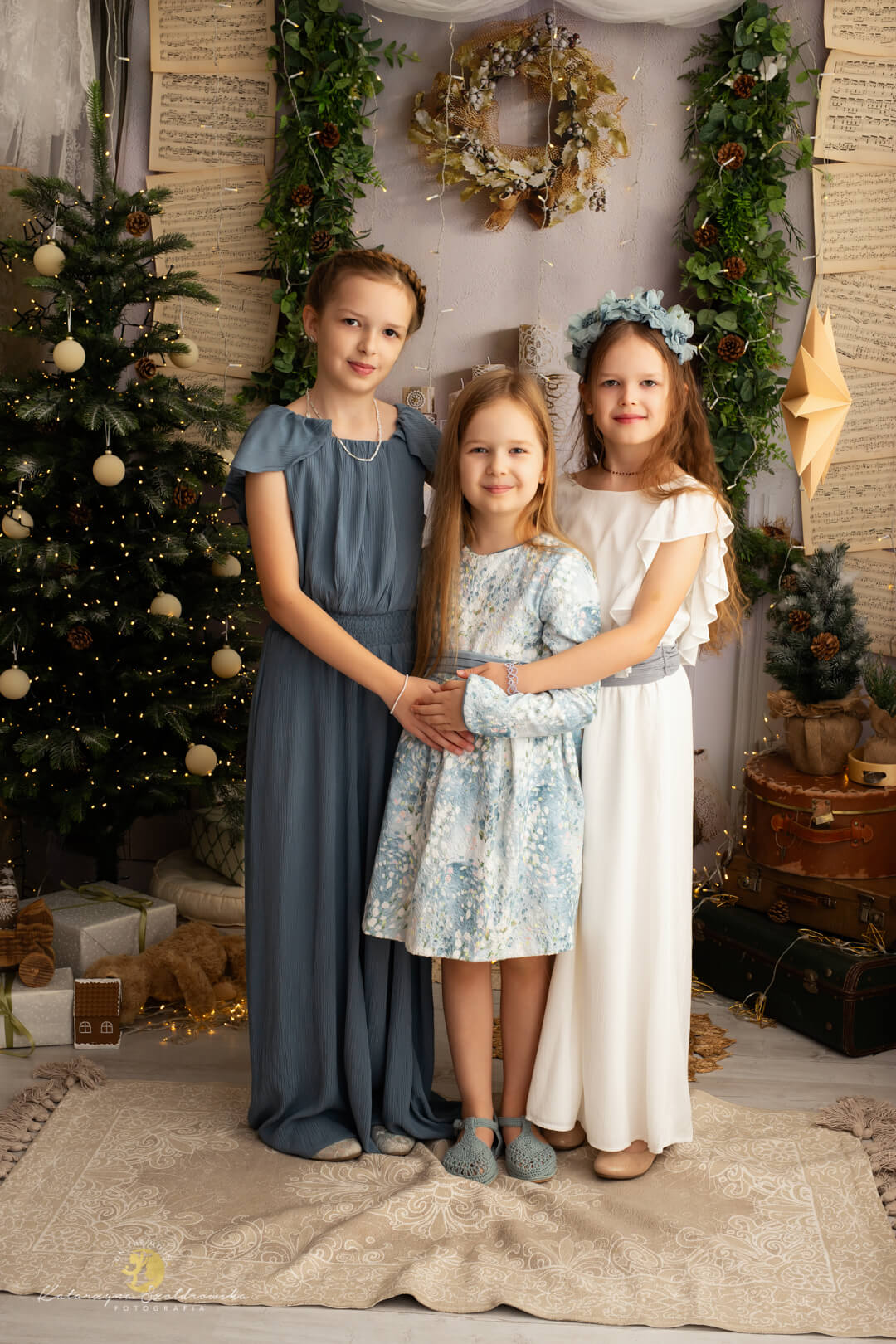 sesja świąteczna kraków. Zdjecie 3 dzieczynek, sióstr, na tle jasnego kominka i choinki